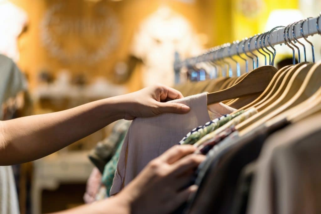 Close up of woman hand choosing thrift young and discount t-shirt clothes in store
