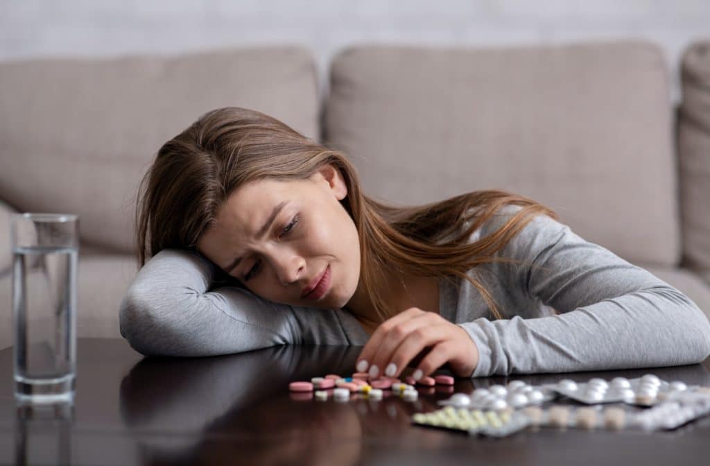 Depressed millennial woman committing suicide by overdosing on sleeping pills, indoors