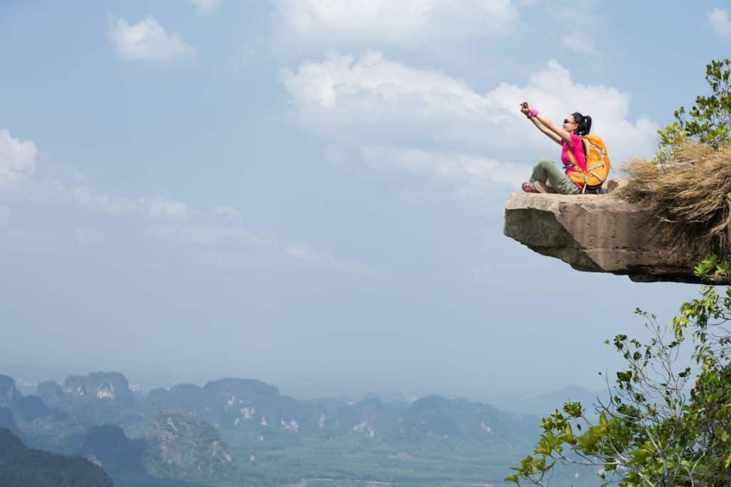 Fearless woman hiker taking selfie on mountain top cliff edge