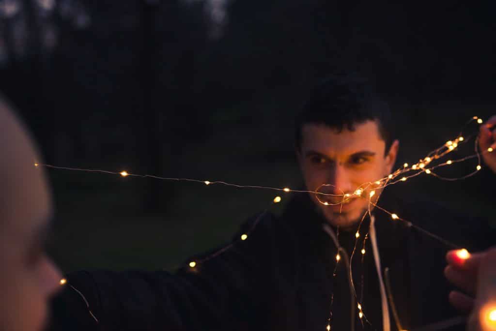 Men unwrapping fairy lights in forest at night