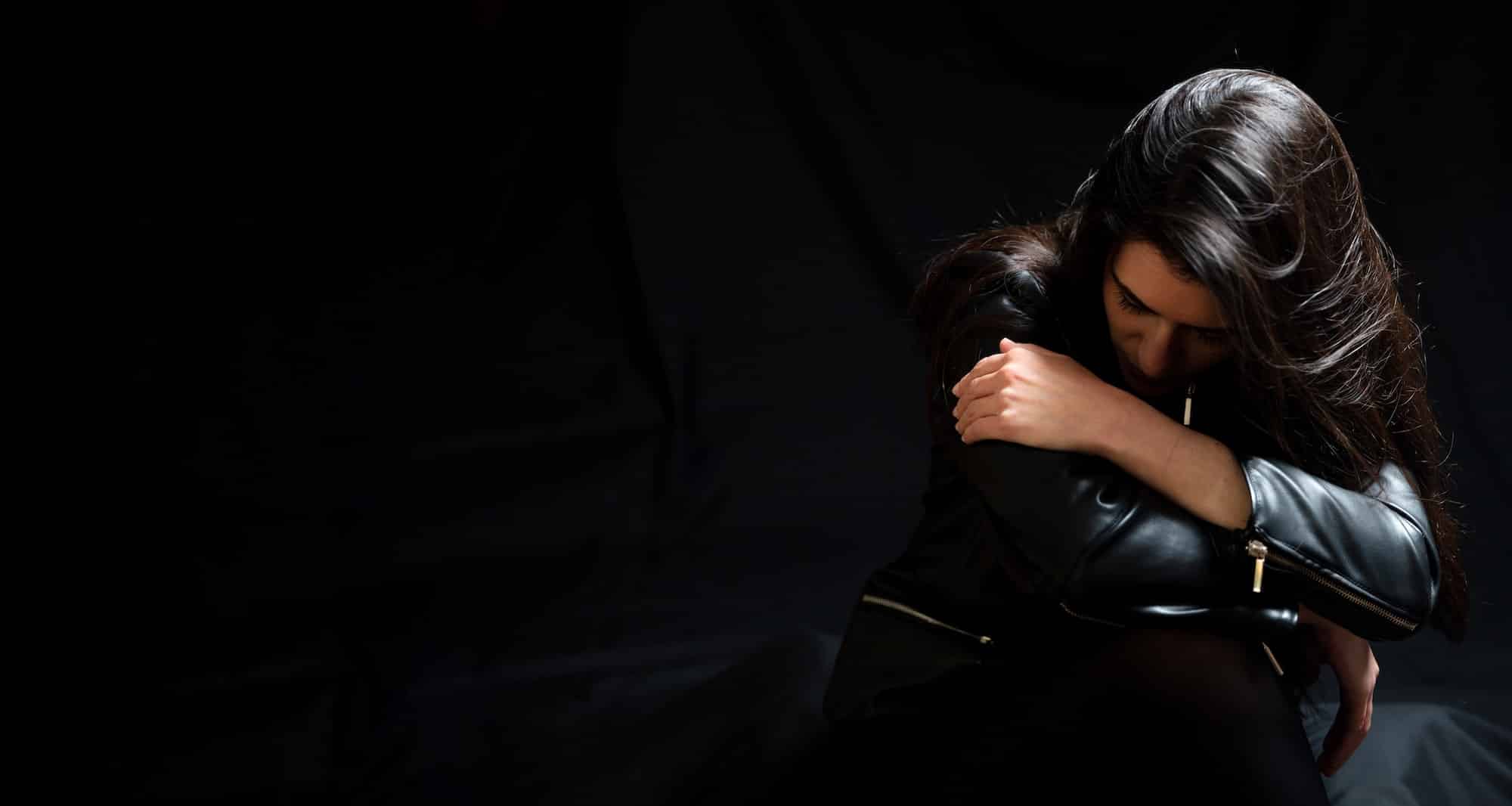 Young woman in a black leather jacket, sad and lonely in a dark room. Depression and grief